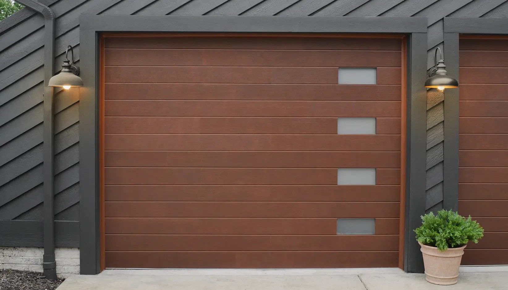 Modern brown garage door with horizontal planks and a vertical row of four frosted glass windows on a dark house exterior.