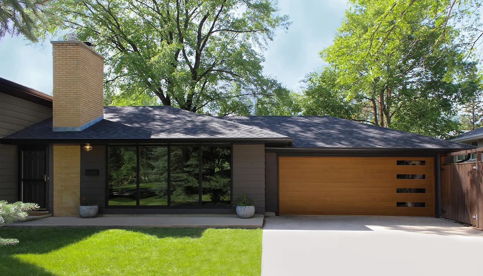 Single-story mid-century modern home with a tan brick chimney, large glass windows, and a horizontal wood garage door.