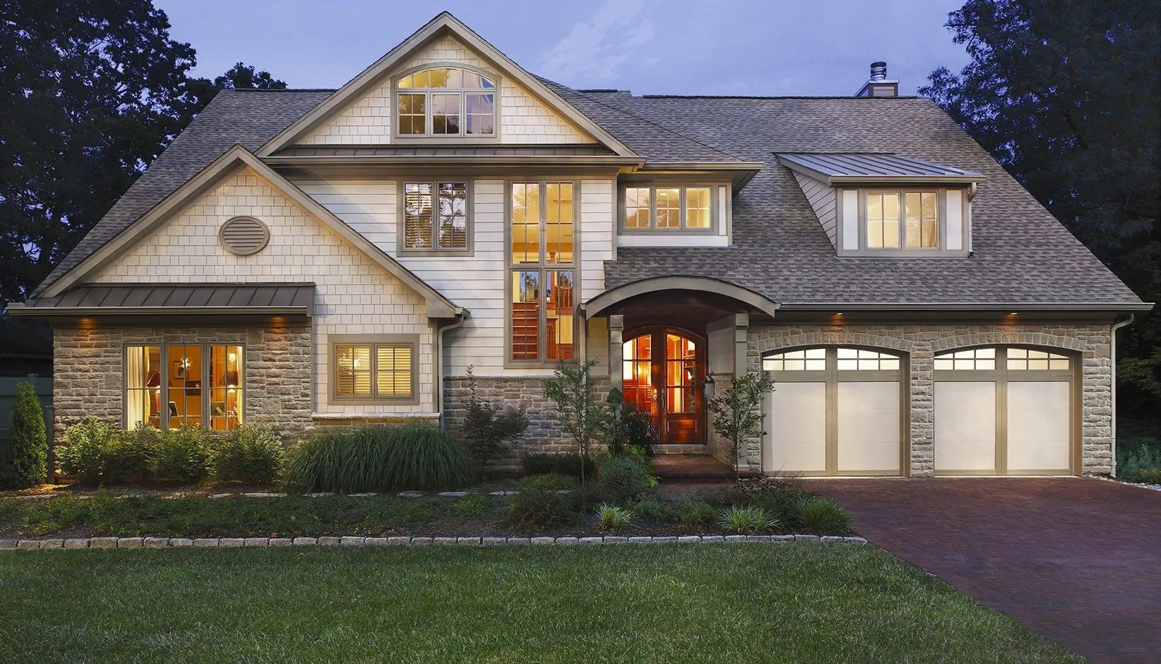 A two-story suburban house with a stone and light-colored siding facade, a two-car garage, and a manicured front lawn.