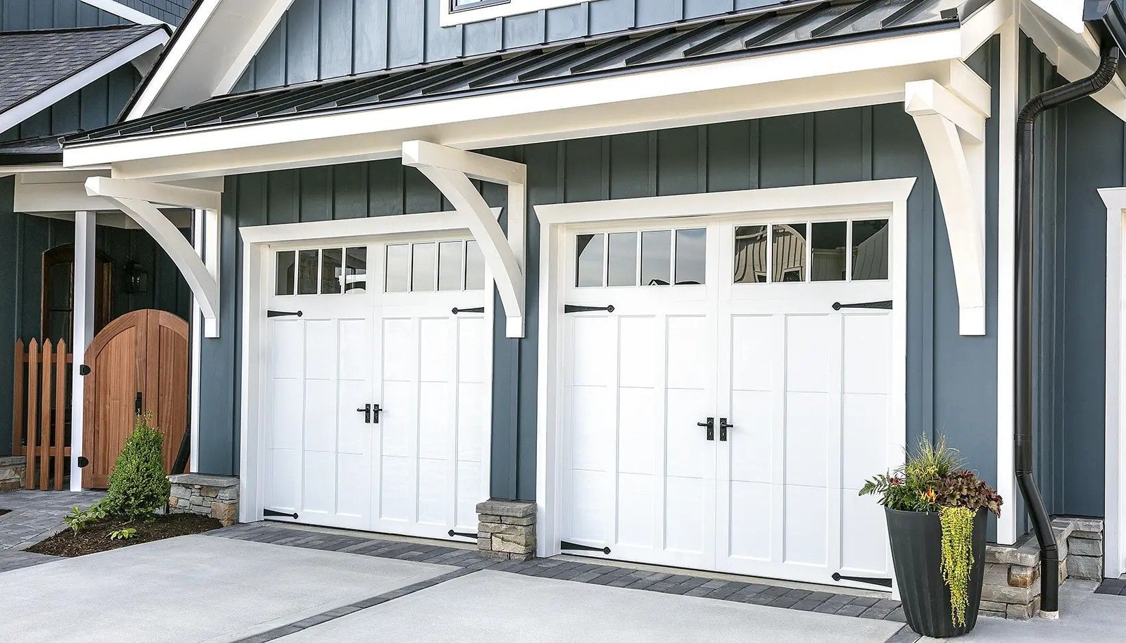 Two white carriage-style garage doors with windows, black hardware, and a matching white wooden roof pergola.