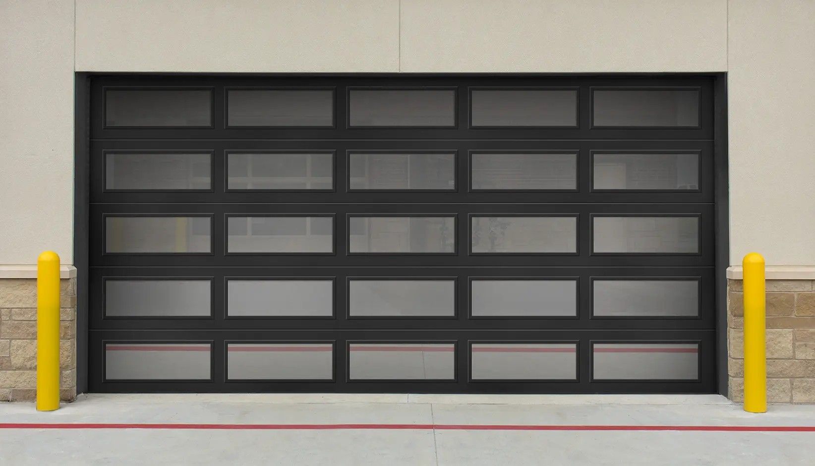A modern black-framed garage door with frosted glass panels sits between two yellow bollards on a concrete driveway.