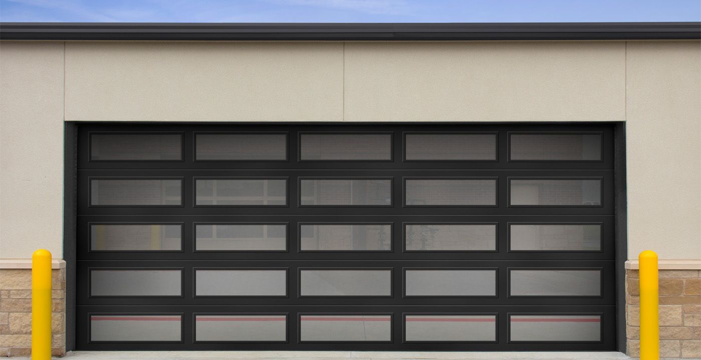 A modern, black-framed garage door with five horizontal rows of frosted glass panels, flanked by yellow safety bollards.