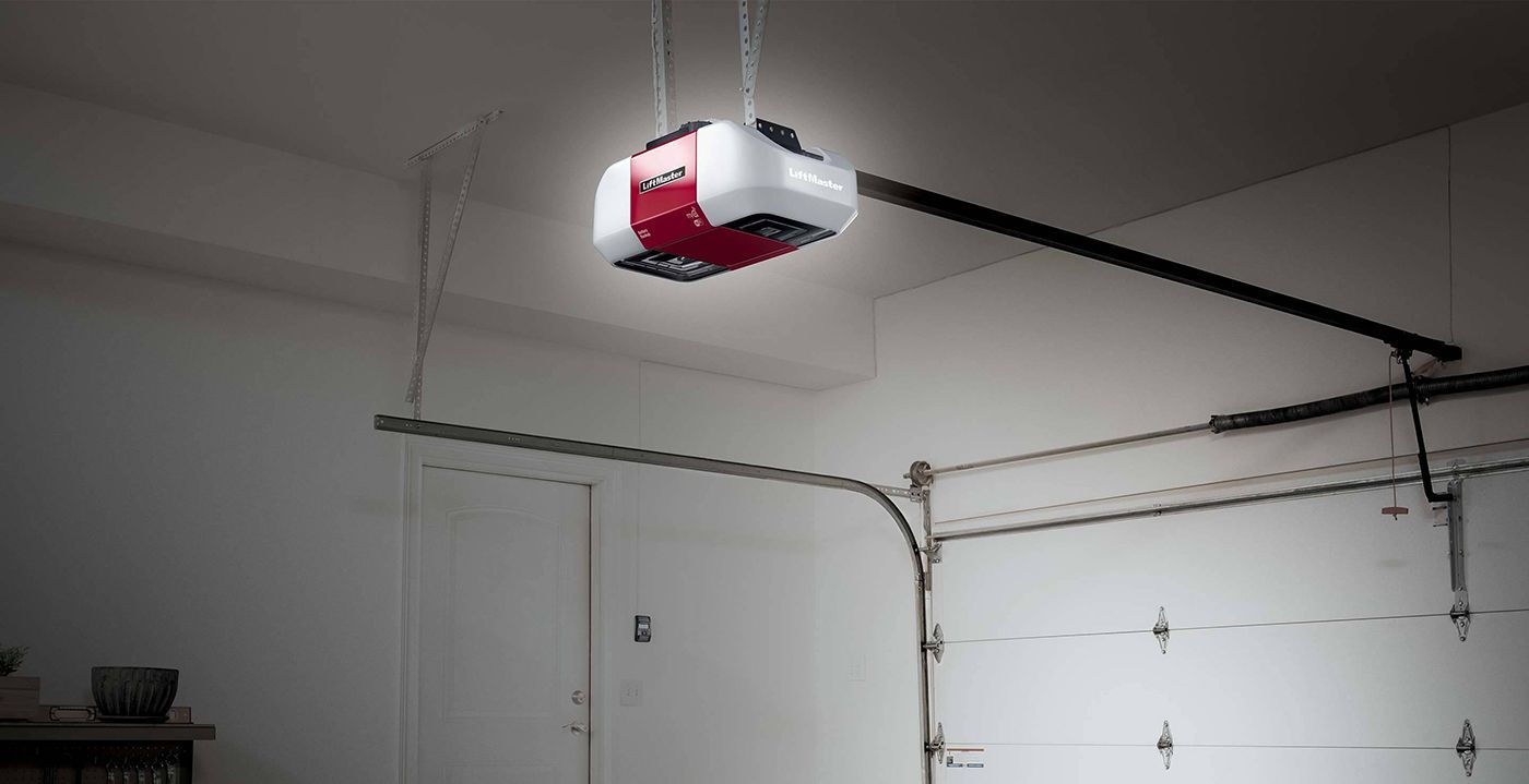 A white and red garage door opener unit mounted to the ceiling with its internal light illuminated.
