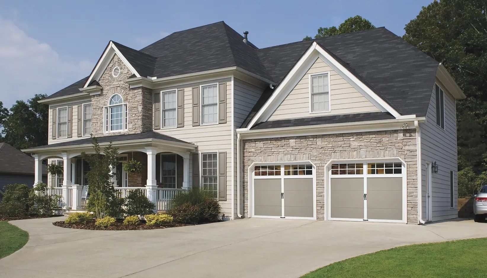 A two-story suburban house with brick and siding, a large front porch, and an attached two-car garage.