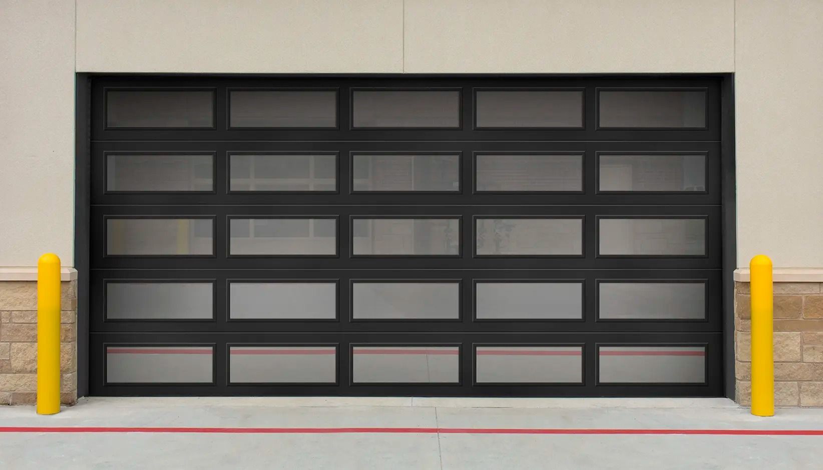 Black garage door in a beige industrial wall, flanked by yellow bollards and a concrete curb.