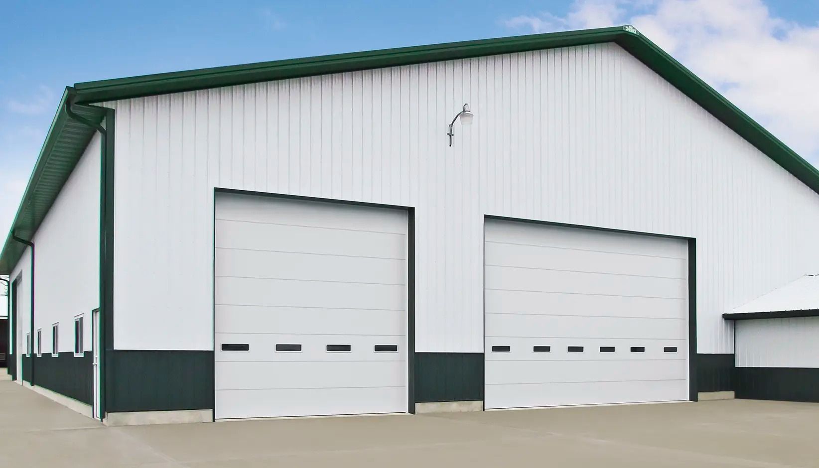 White metal warehouse with two large garage doors and green trim under a blue sky.