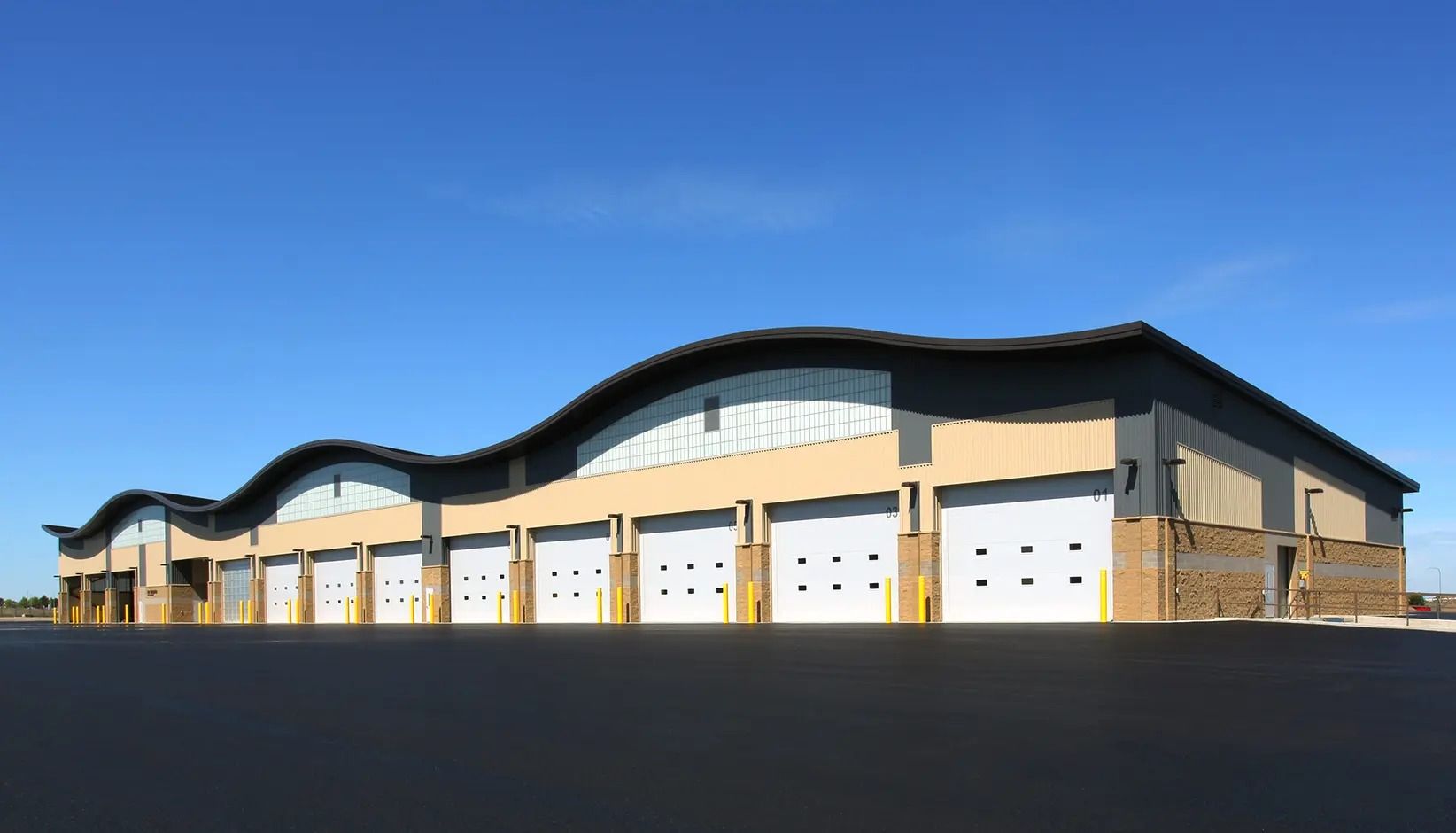 Large beige industrial building with multiple garage doors under a blue sky