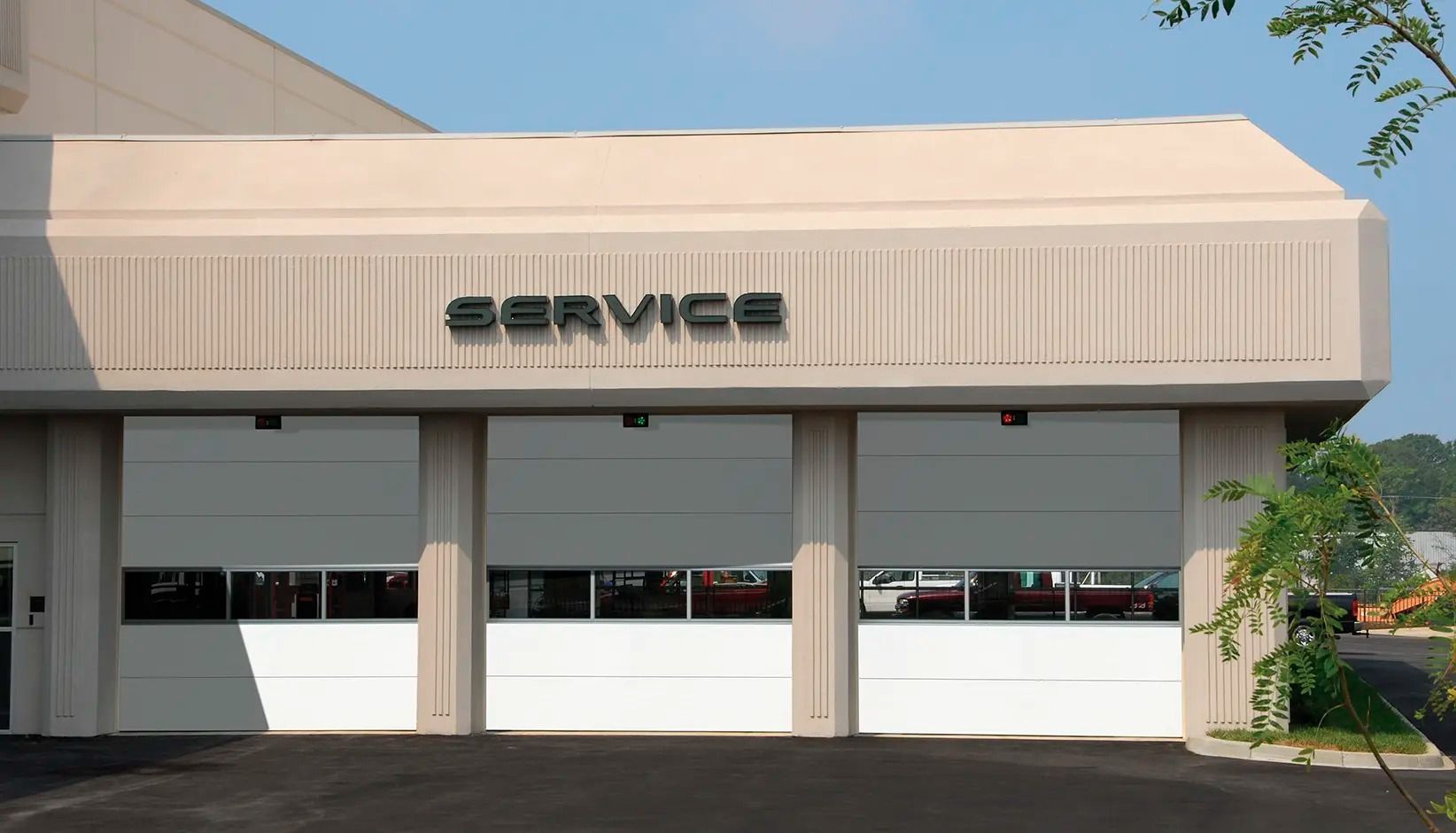 Auto service building with a beige awning, three garage doors, and a “SERVICE” sign above the entrance.