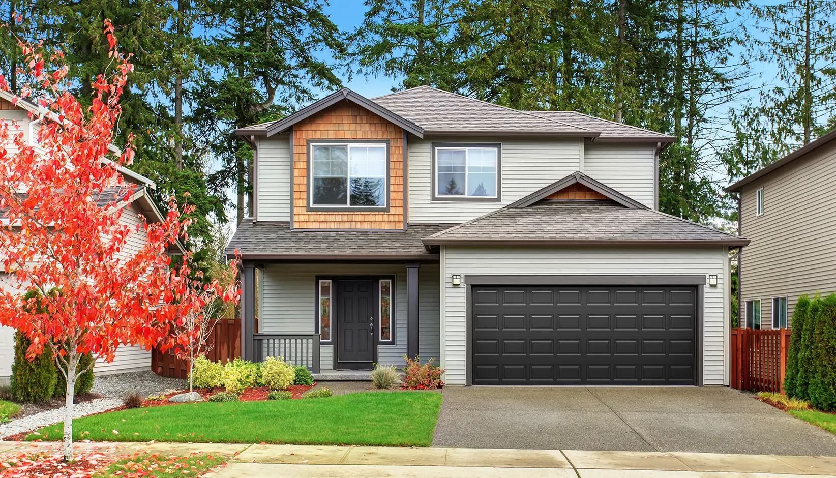 Two-story suburban house with black garage door, red tree, and front lawn