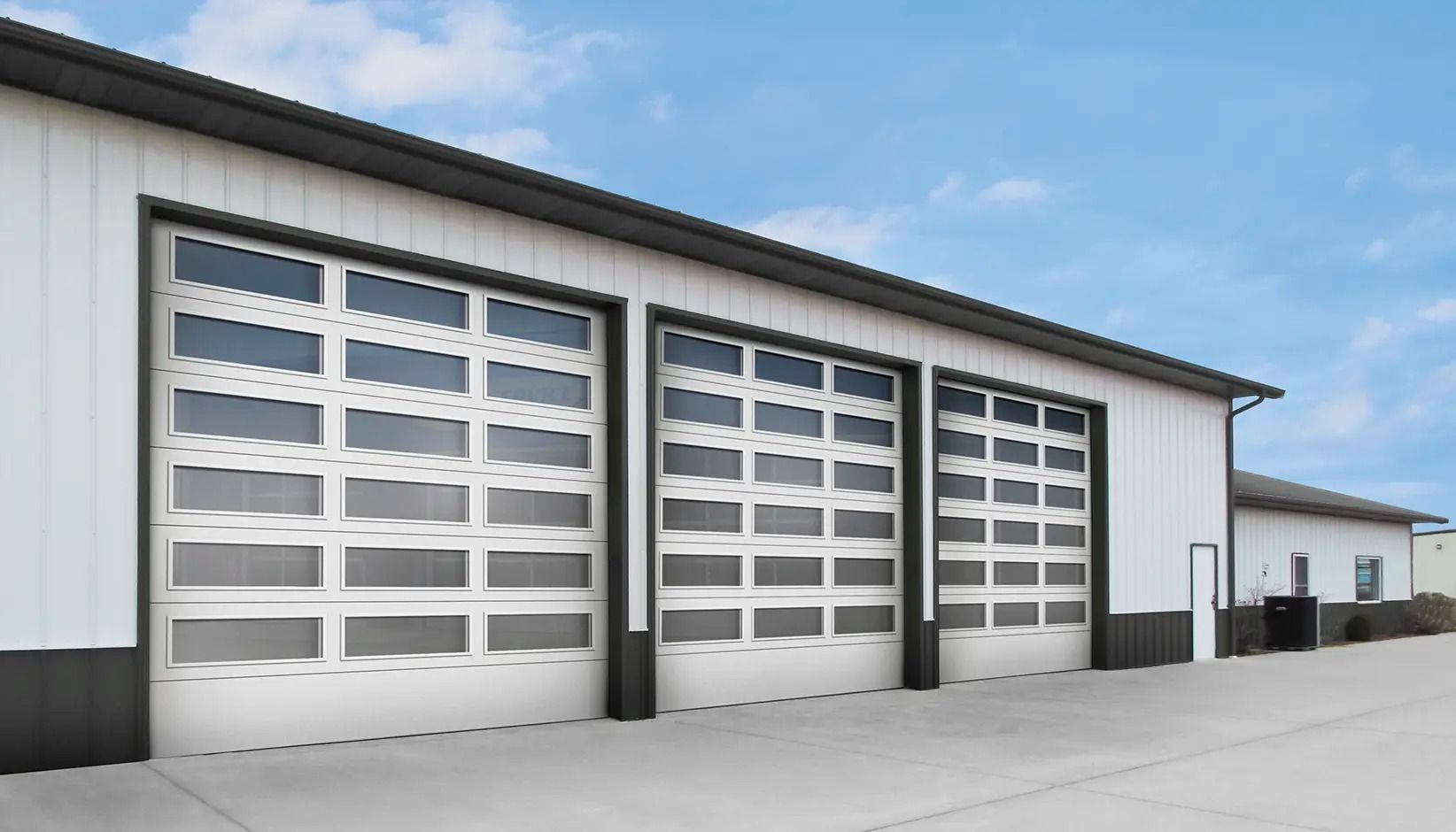 Three white garage doors on a light gray industrial building under a blue sky