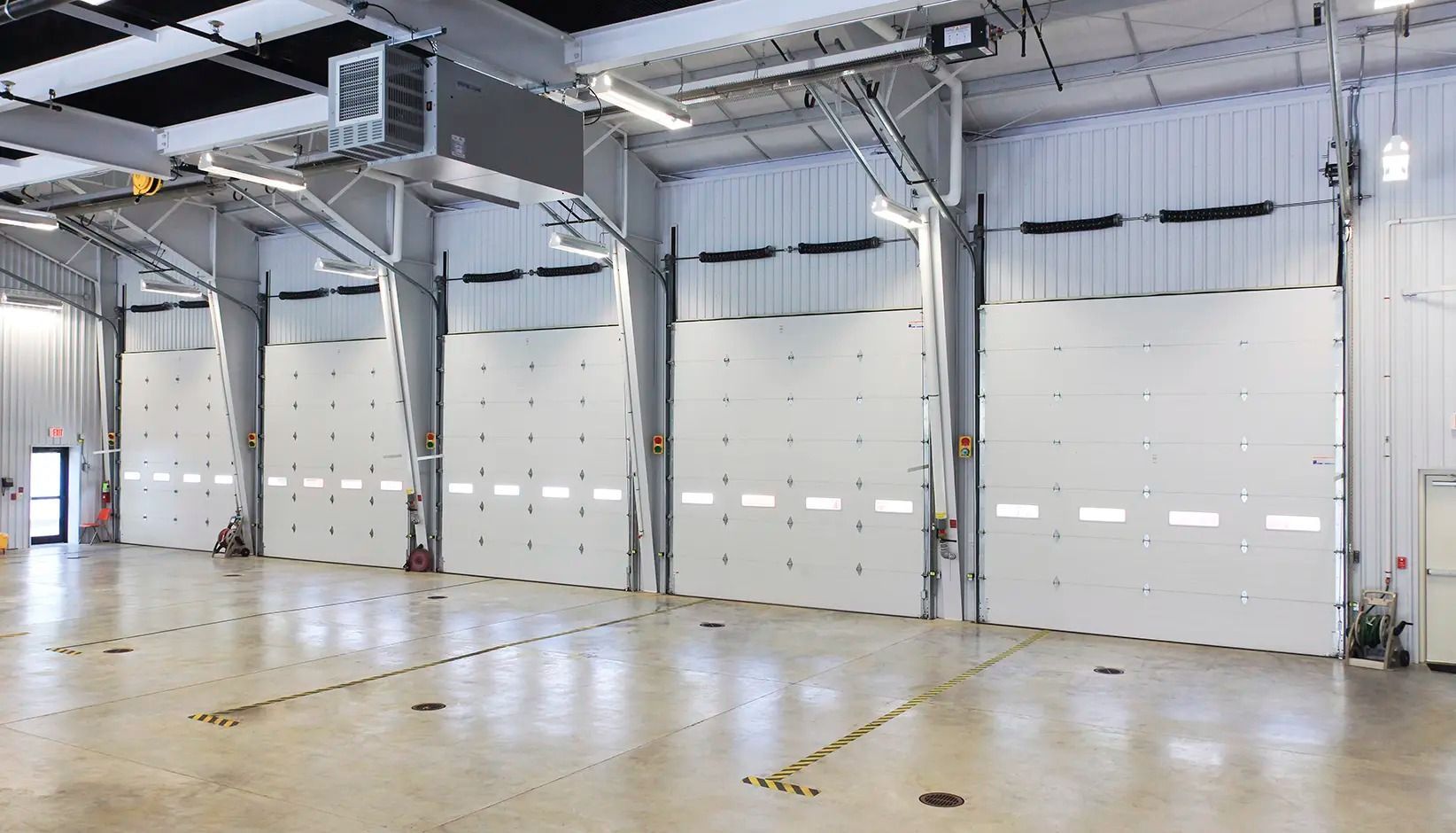 Empty industrial warehouse with large white roll-up doors and polished concrete floor