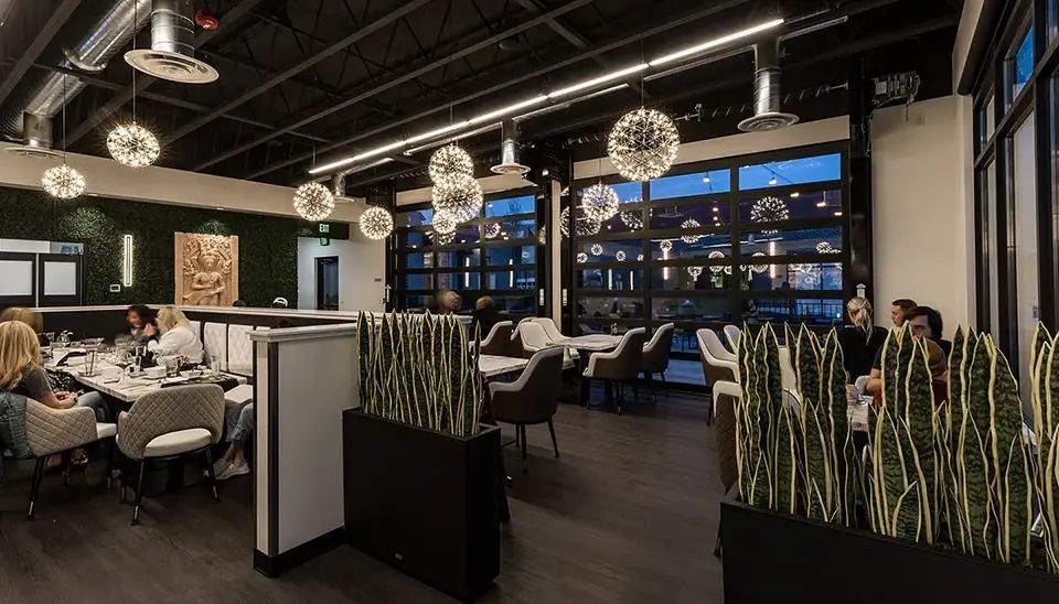 Modern restaurant interior with tables, lounge seating, hanging globe lights, and large windows at night