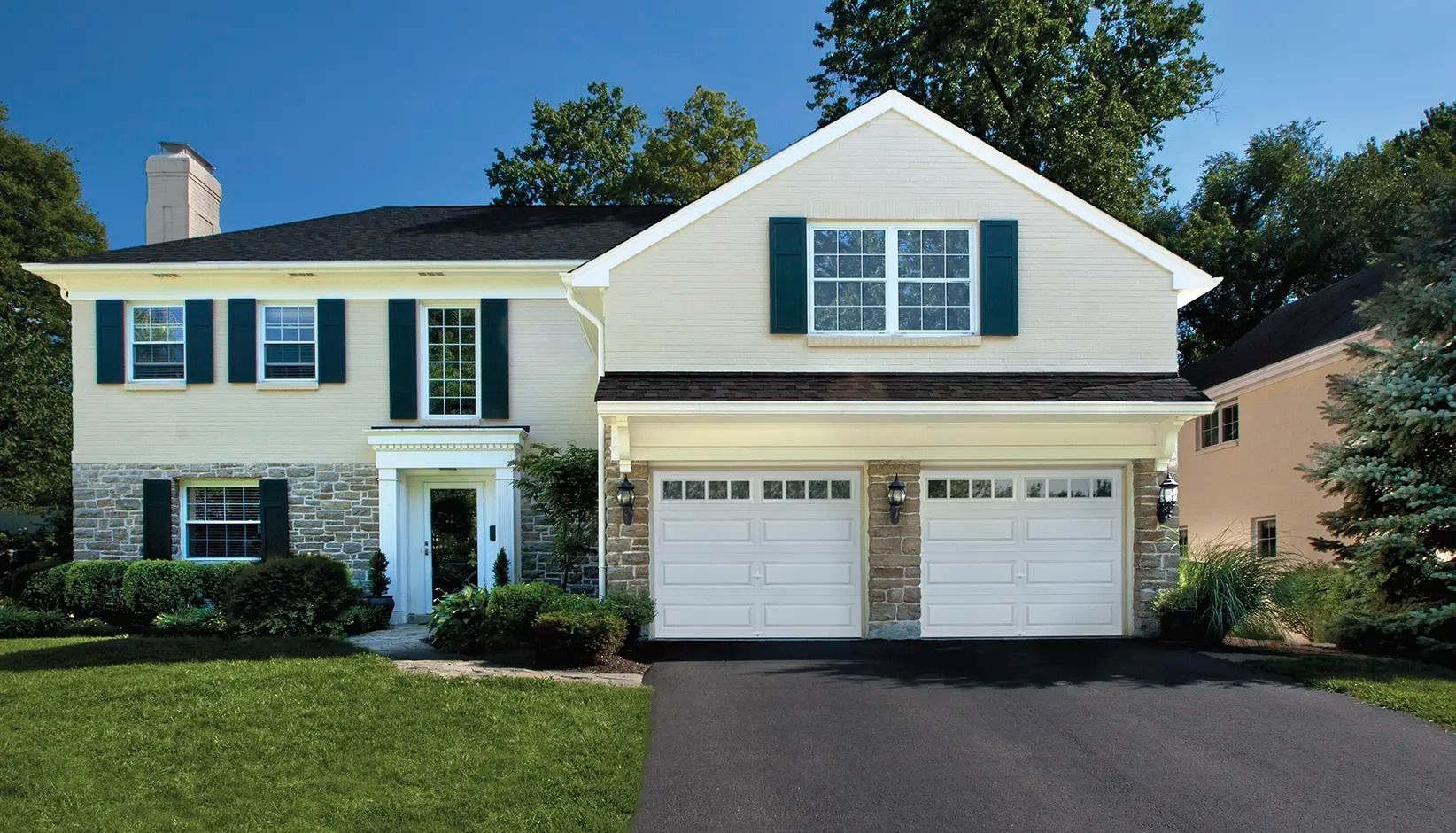 Two-story white suburban house with black shutters, a double garage, and a green lawn