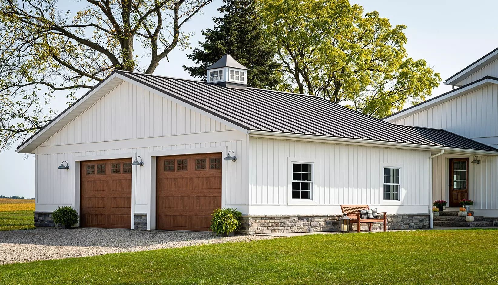 White single-story house with two brown garage doors, white trim, and a green lawn under trees