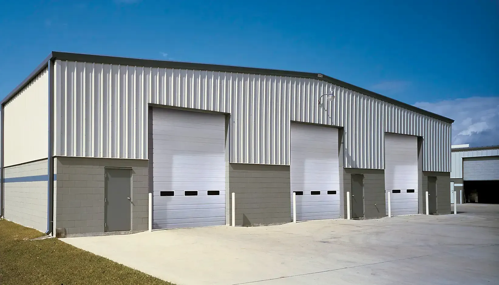 Metal industrial warehouse with three garage doors and a small side door under a blue sky