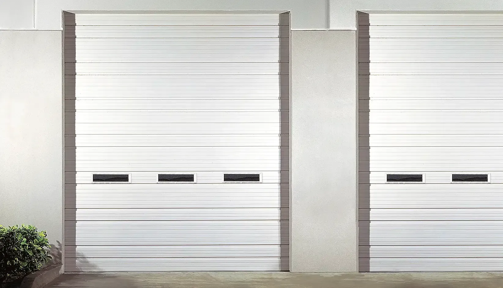 Two white roll-up garage doors on a light gray industrial building