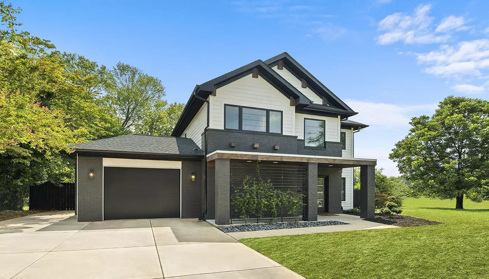 A two-story house with a grey brick exterior, white siding, a black garage door, and a covered front porch.