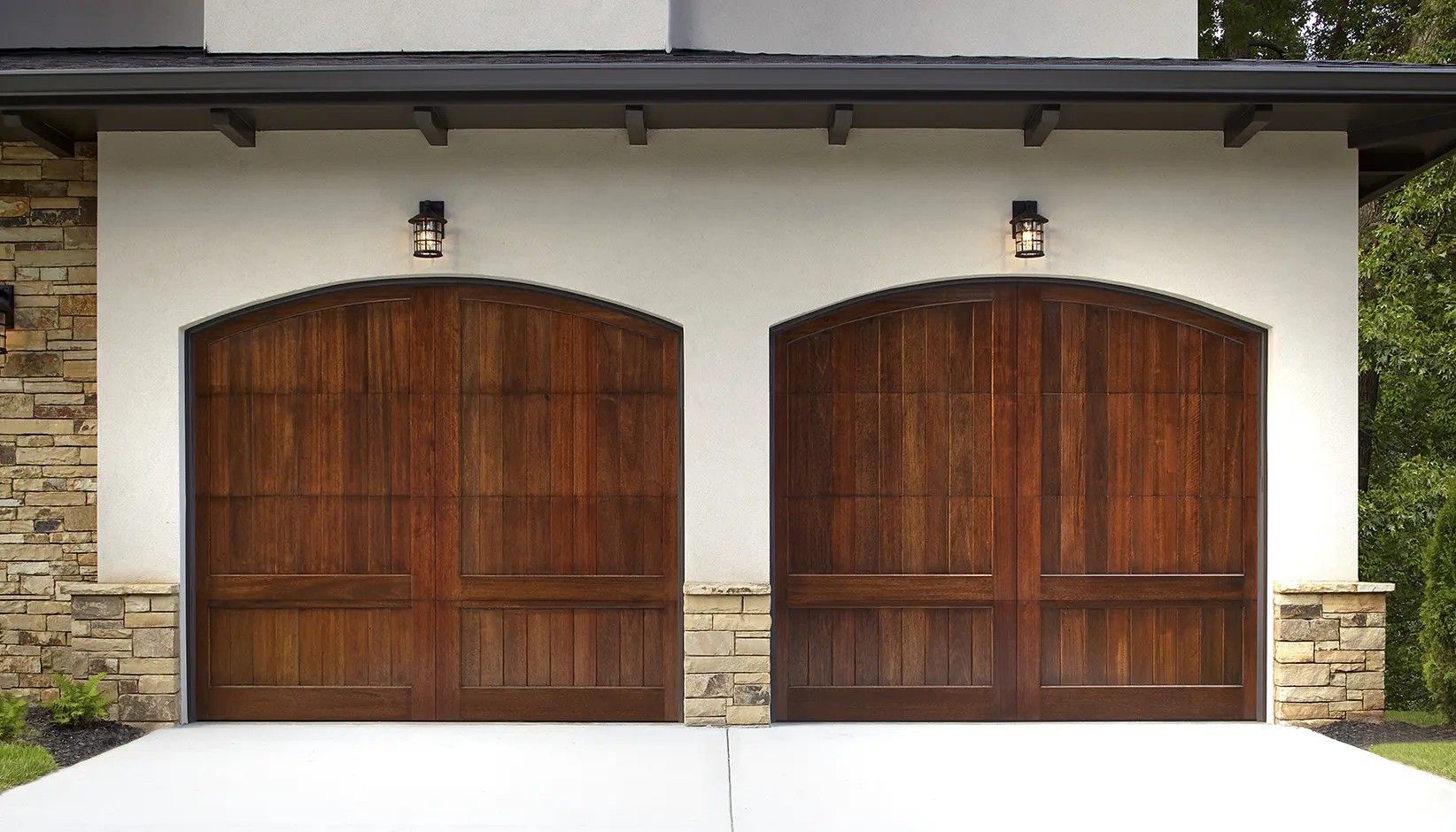 Two dark wood, arched-top garage doors on a white stucco home with stone accents.