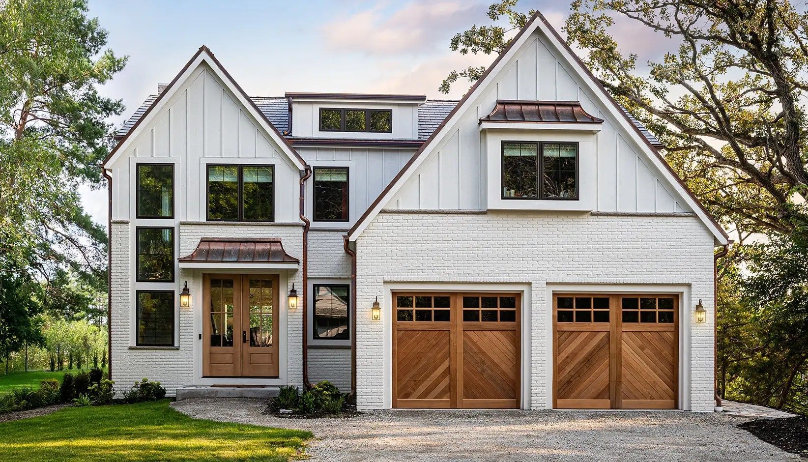 A modern two-story home with white board-and-batten siding, stone accents, two wooden garage doors, and a front porch.