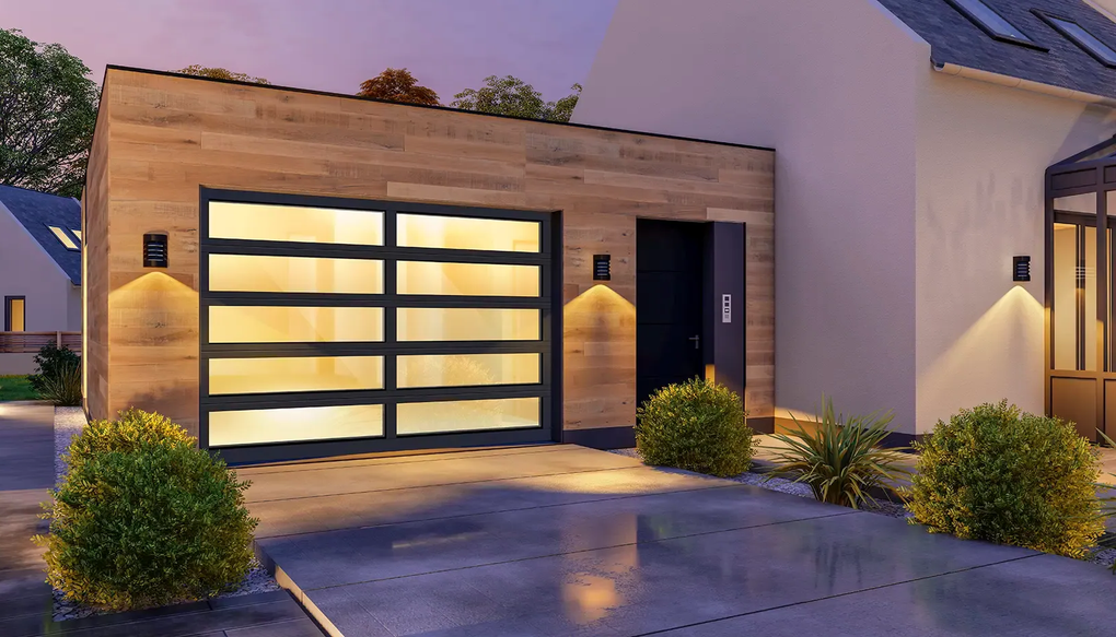 A modern garage with horizontal wood siding, a glass sectional door, and warm outdoor lighting at twilight.