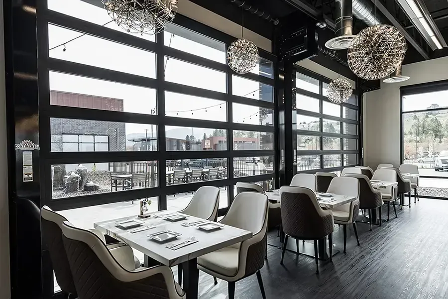 Modern restaurant interior with large windows, white table settings, and hanging globe lights