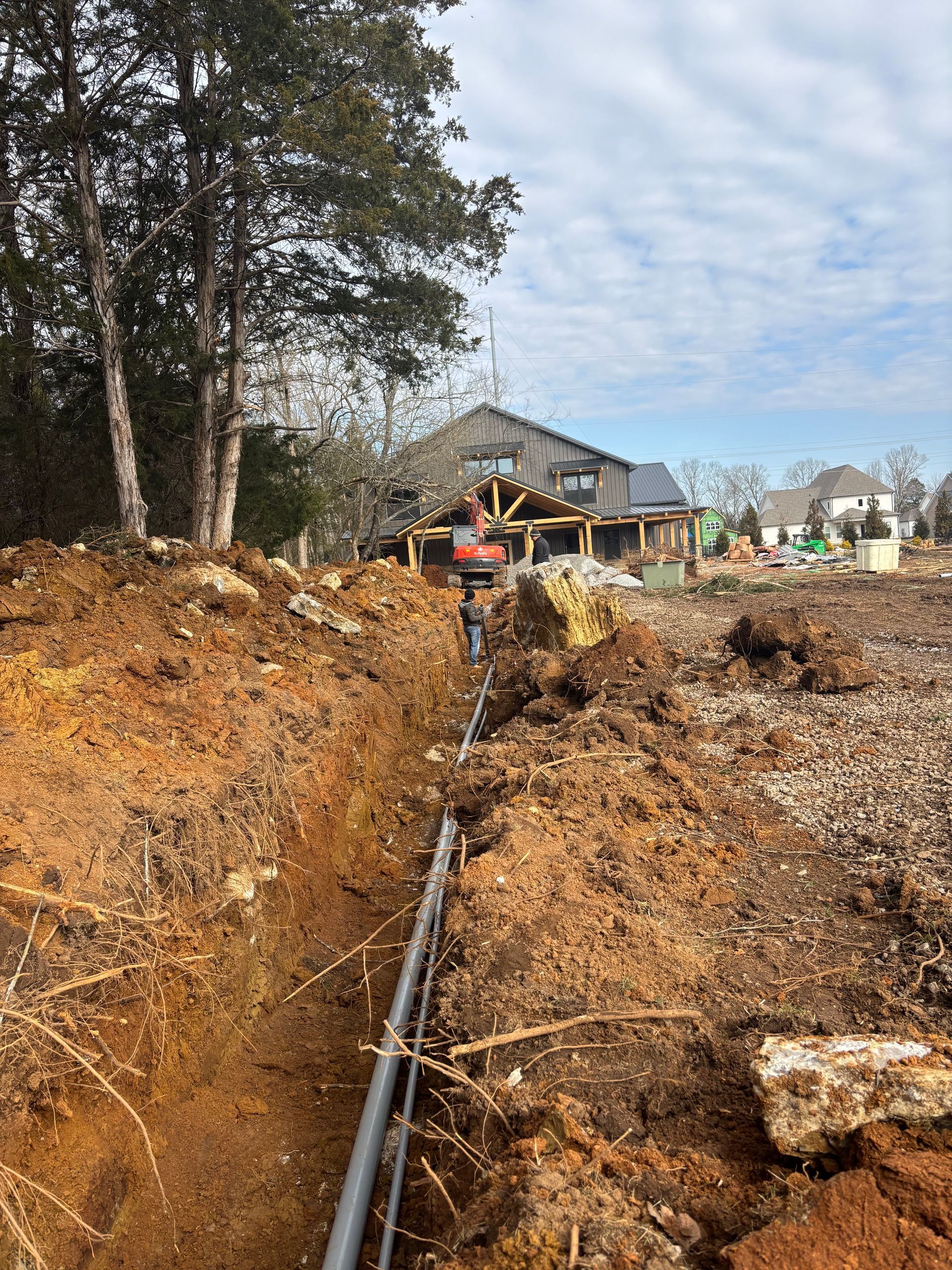 A pipe is being installed in the dirt in front of a house.