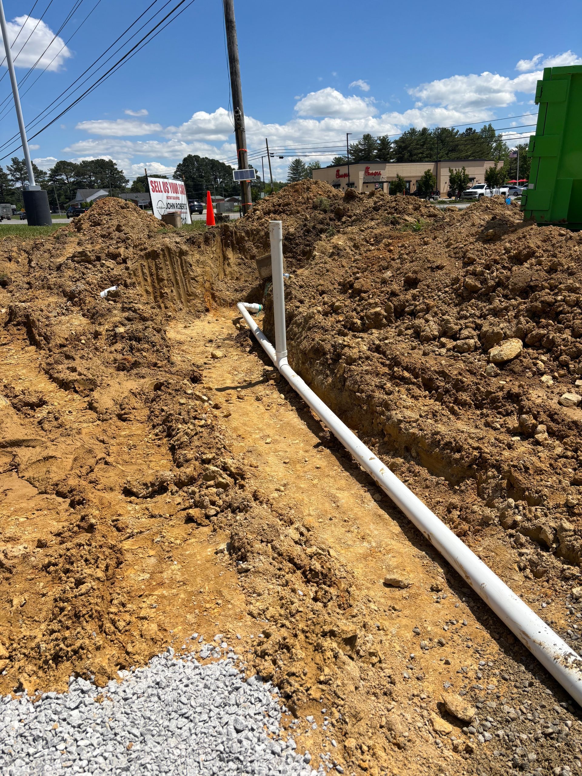 A white pipe is laying in the dirt next to a pile of dirt.