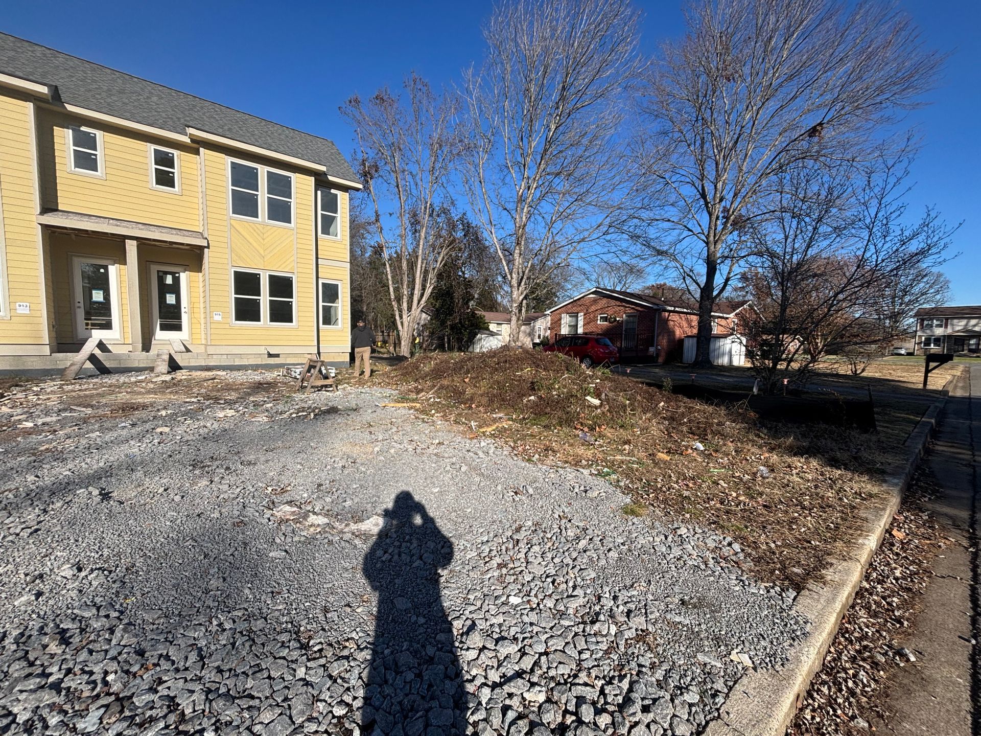 A shadow of a person is cast on a gravel driveway in front of a house.