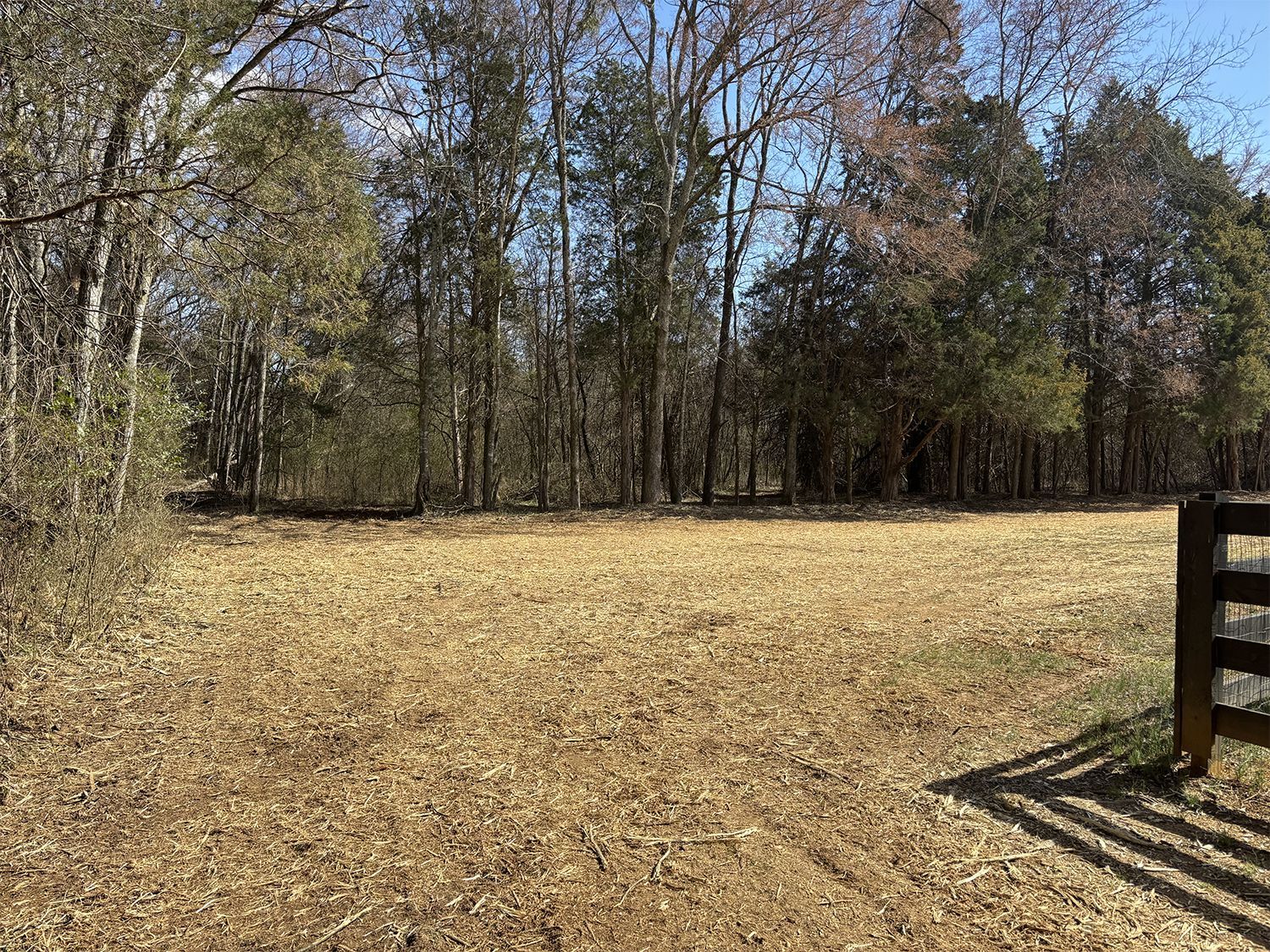 There is a fence in the middle of a field with trees in the background.