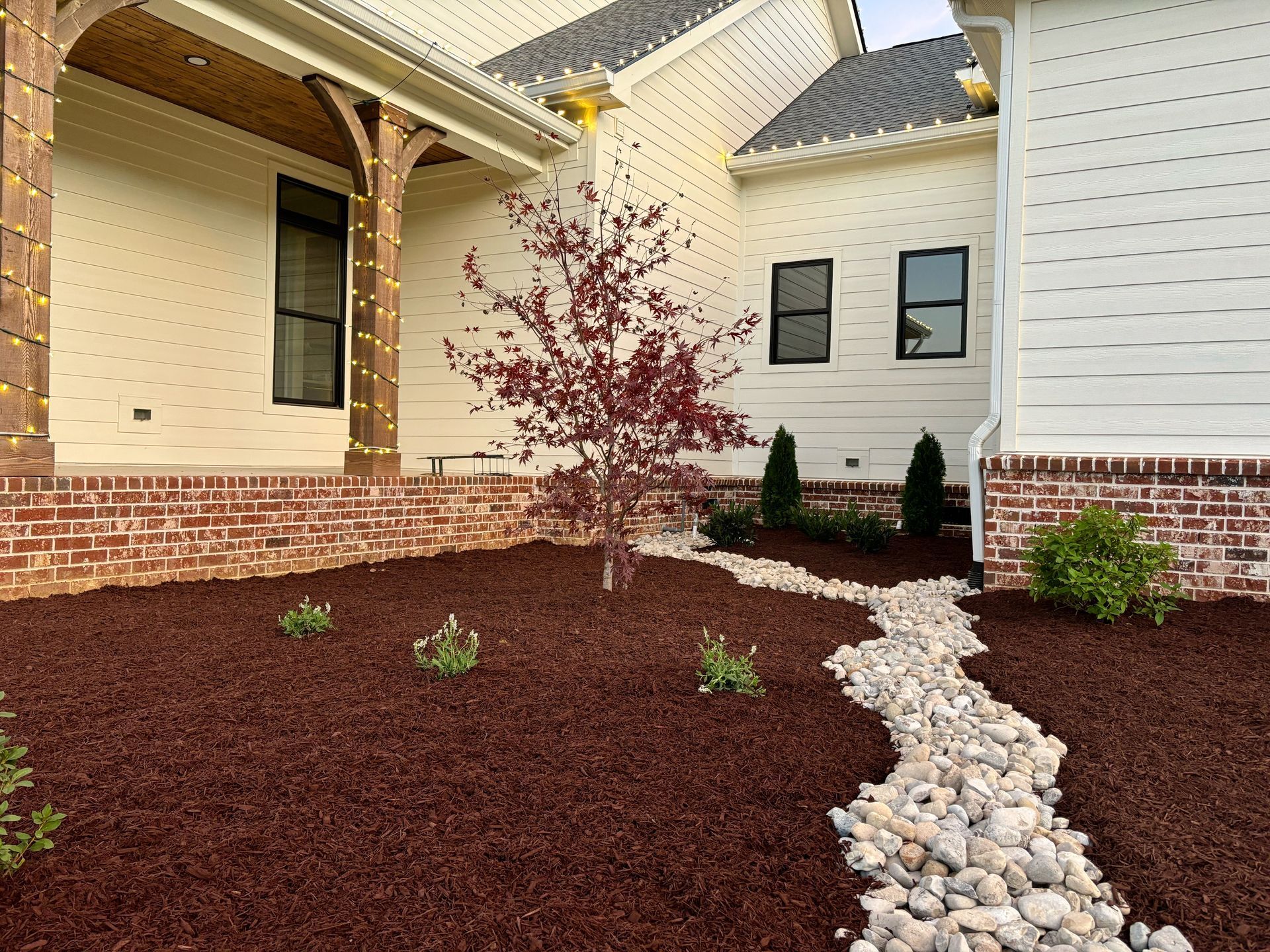 A white house with a brick wall and a tree in front of it.