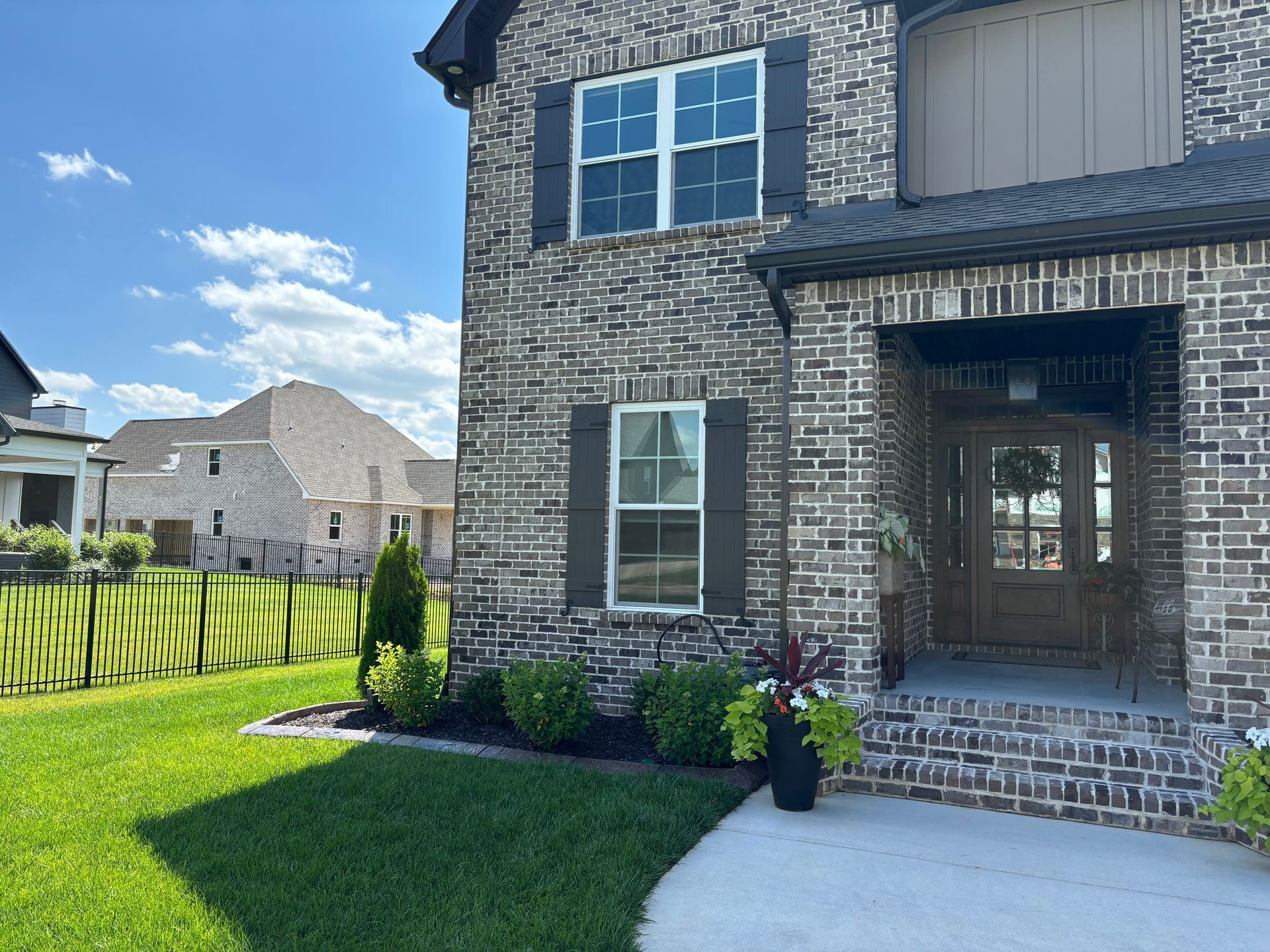 A large brick house with a porch and a fence in front of it.