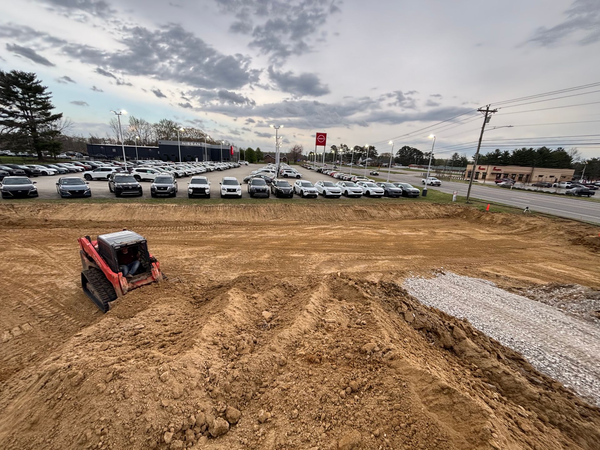 A bulldozer is working on a dirt field in front of a parking lot.