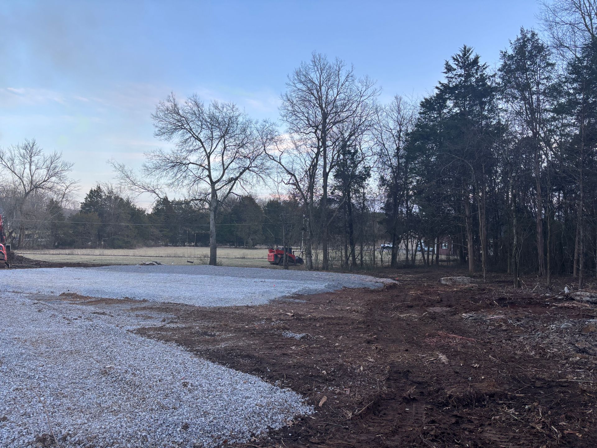 A snowy field with trees in the background and a tractor in the foreground.