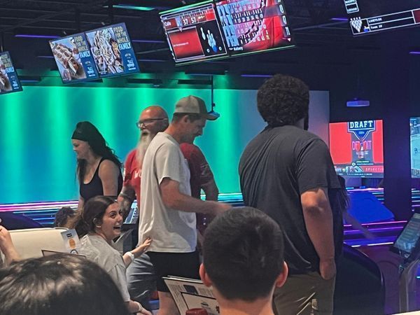 People bowling in an alley with screens displaying scores. Green and blue lighting. Some people are reacting with excitement.