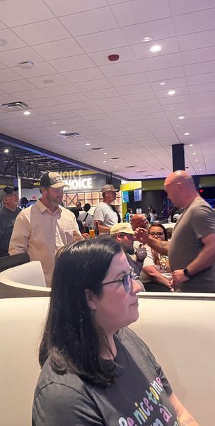 People in a brightly lit entertainment venue. A woman sits, others stand, some wearing hats.