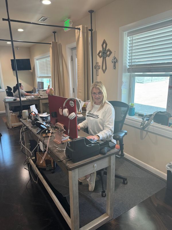 Woman sitting at a desk in an office, working on a computer. Beige walls, window, cross decor.