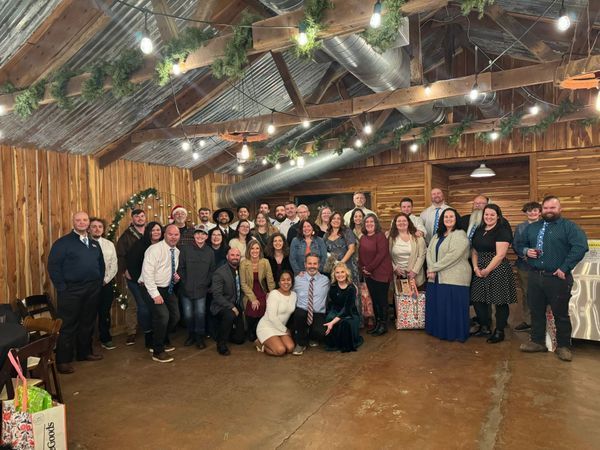 Group of people indoors, celebrating. Rustic setting, string lights, some wearing formal attire.