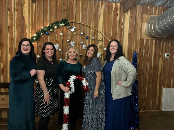 Five people smiling near holiday decorations, posing at an event.