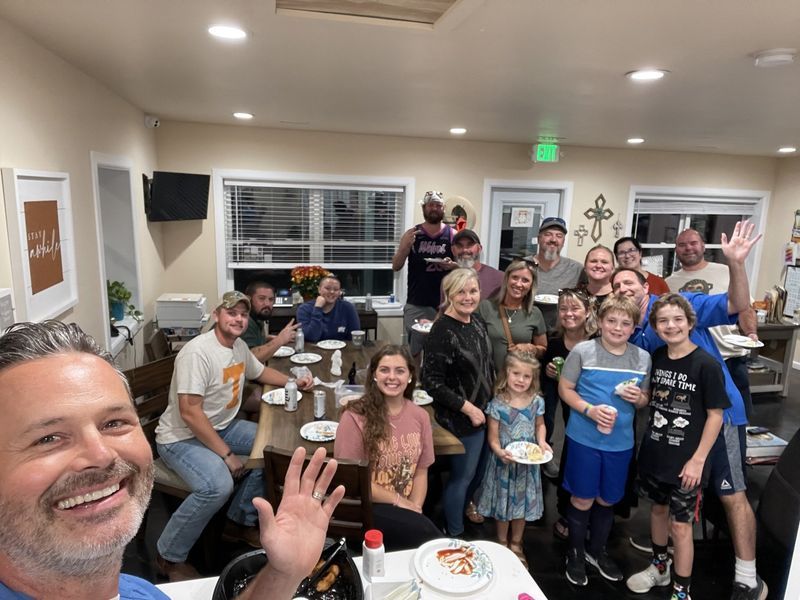 Group of people gathered around tables in a room, some waving and smiling.