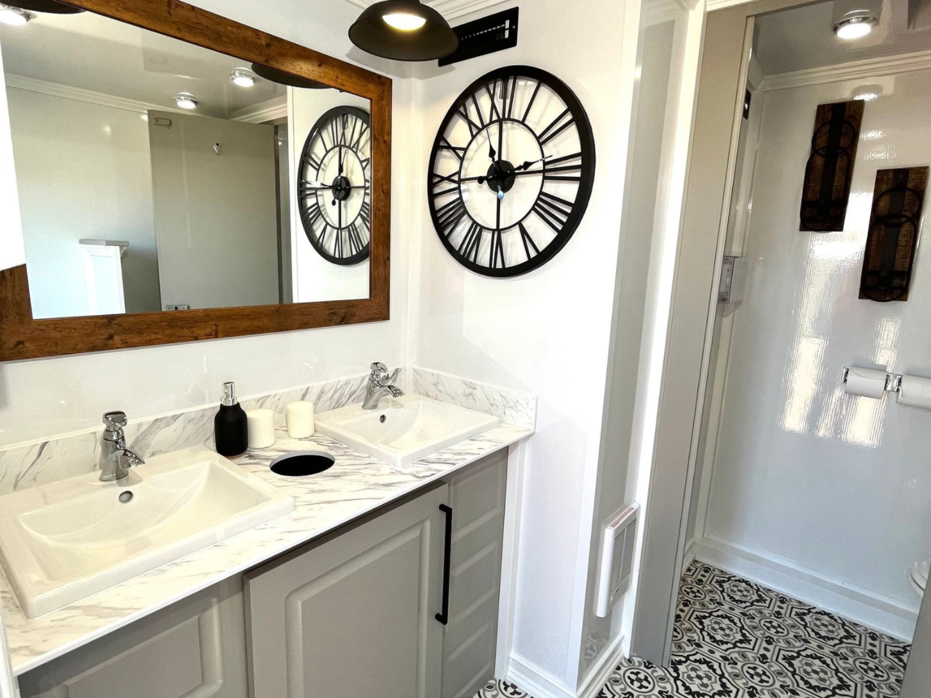 Bathroom interior with double sinks, large mirror, decorative clock, and patterned floor.