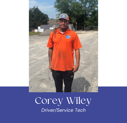 Man in orange polo shirt and baseball cap standing outdoors. Name is Corey Wiley, Driver/Service Tech.