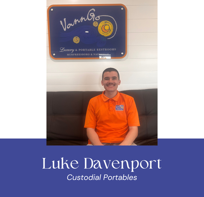 Man in orange shirt sits in front of a sign that reads 