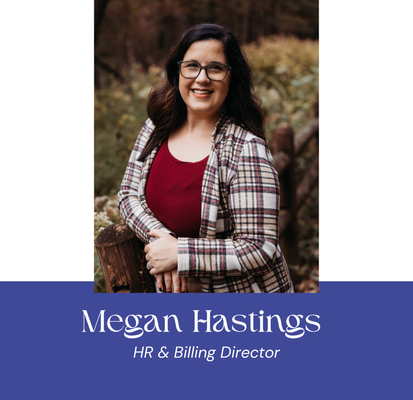 Megan Hastings, HR & Billing Director, smiles wearing glasses and plaid jacket, standing outdoors near wood and foliage.