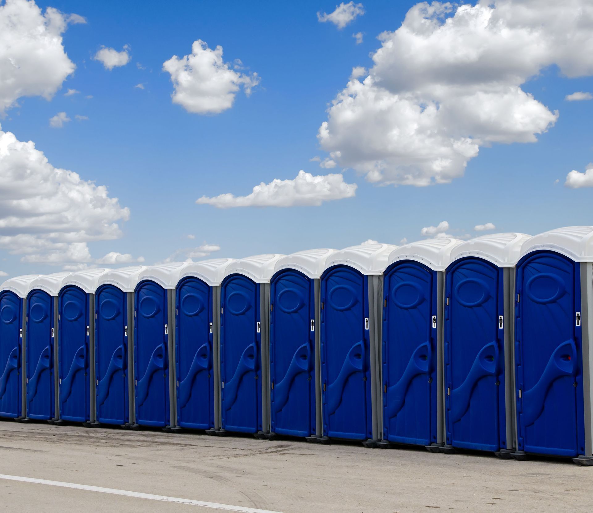 Row of blue portable toilets under a partly cloudy sky.