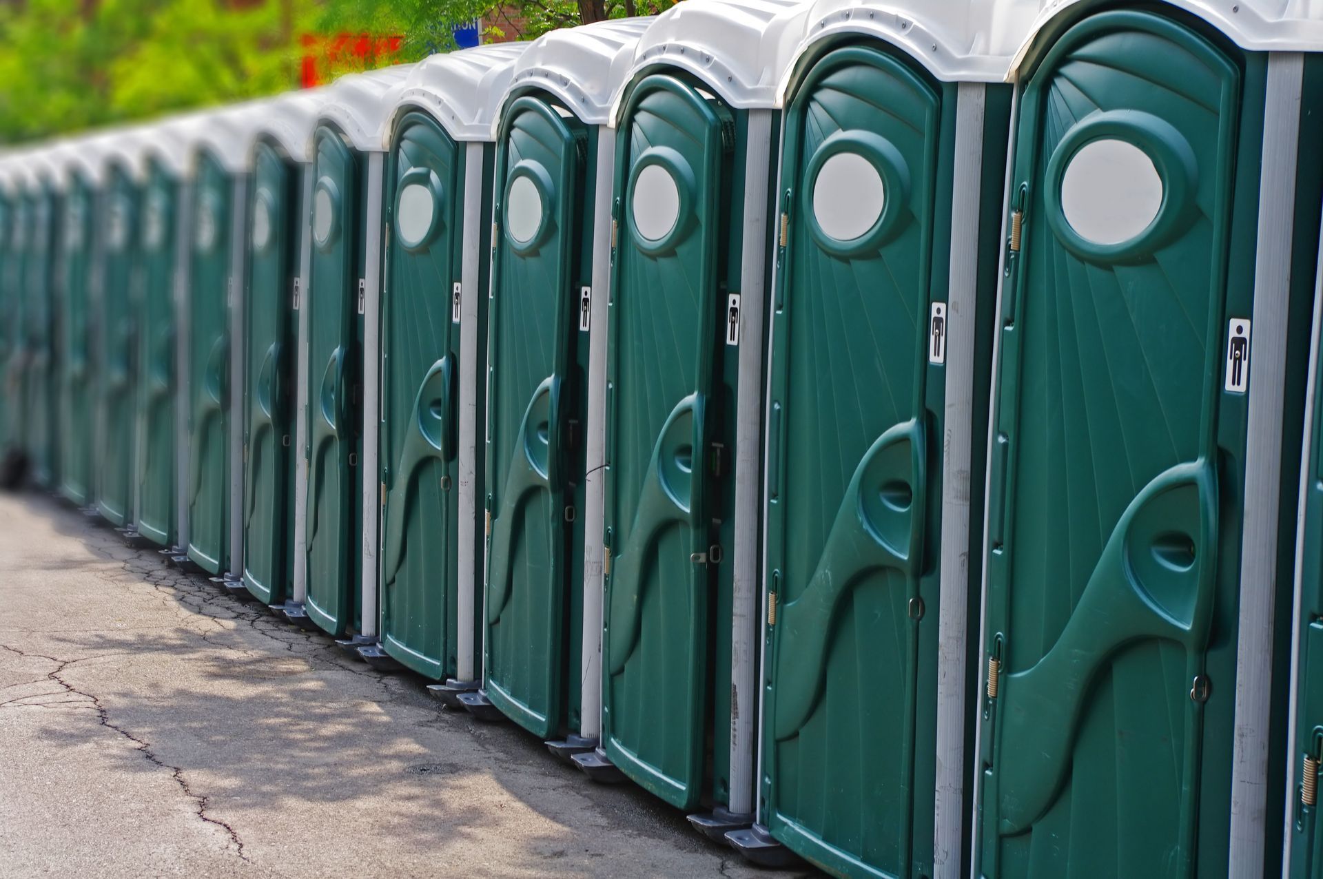 Row of green portable toilets lined up outdoors.