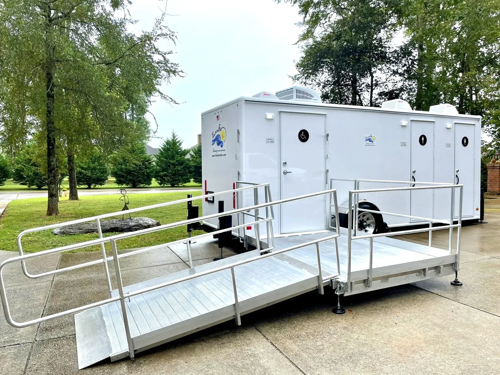White portable restroom trailer with ramp for accessibility on a paved area, outdoors.