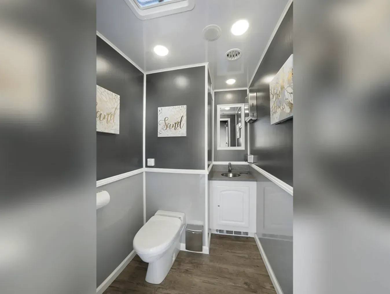 Interior of a modern portable restroom with grey walls, white trim, a toilet, and a sink.