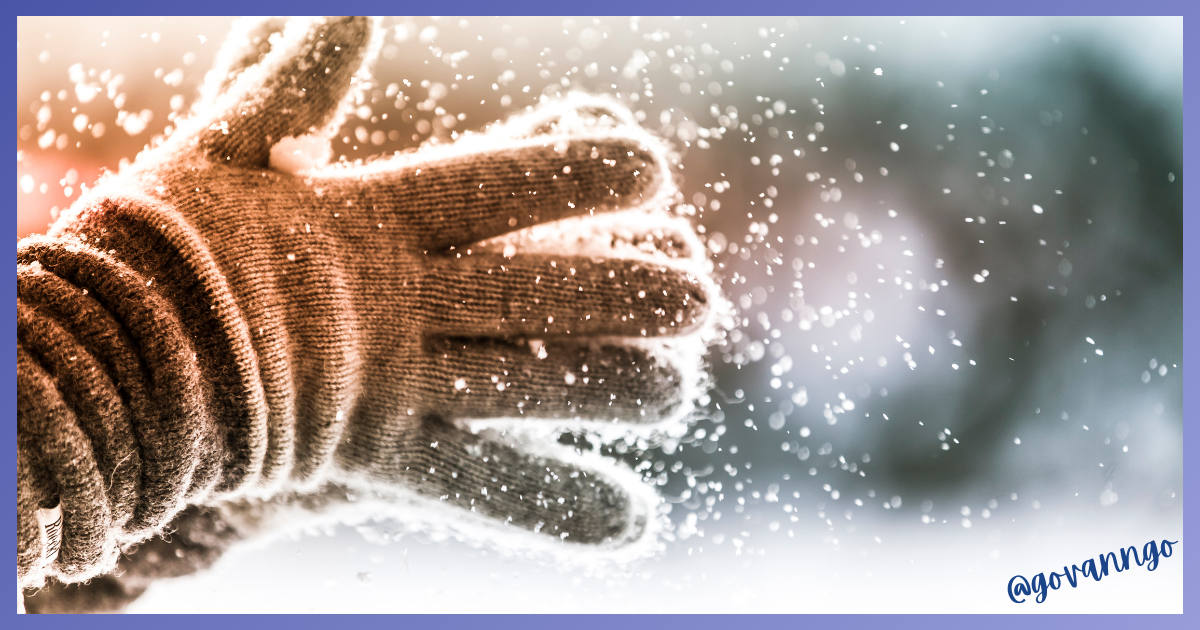 Gloved hands forming a snowball with falling snow, outdoors.