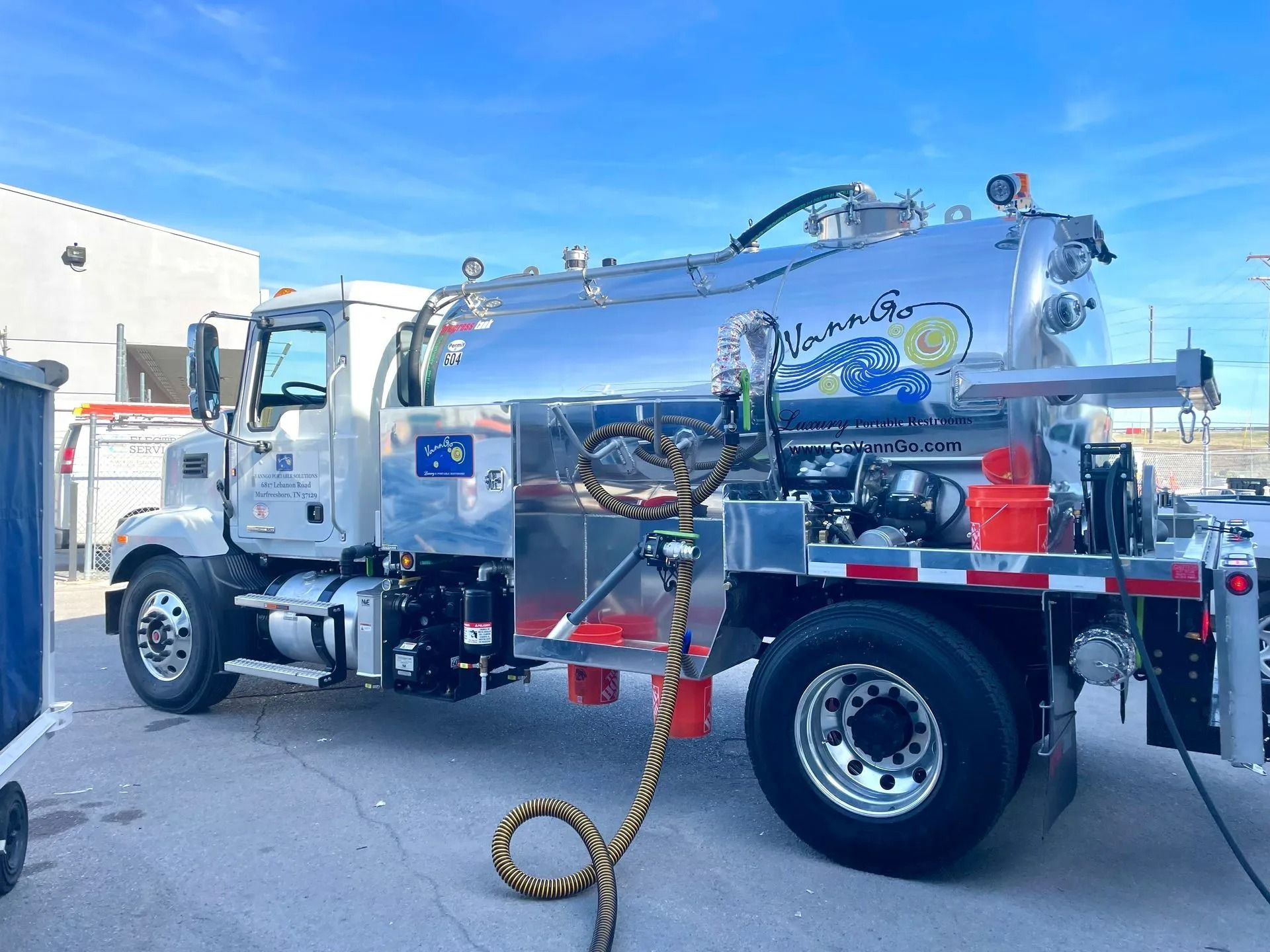 A white septic tanker truck parked on pavement against a bright blue sky