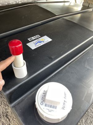 A person’s finger pointing at a red-capped pipe on a black plastic tank